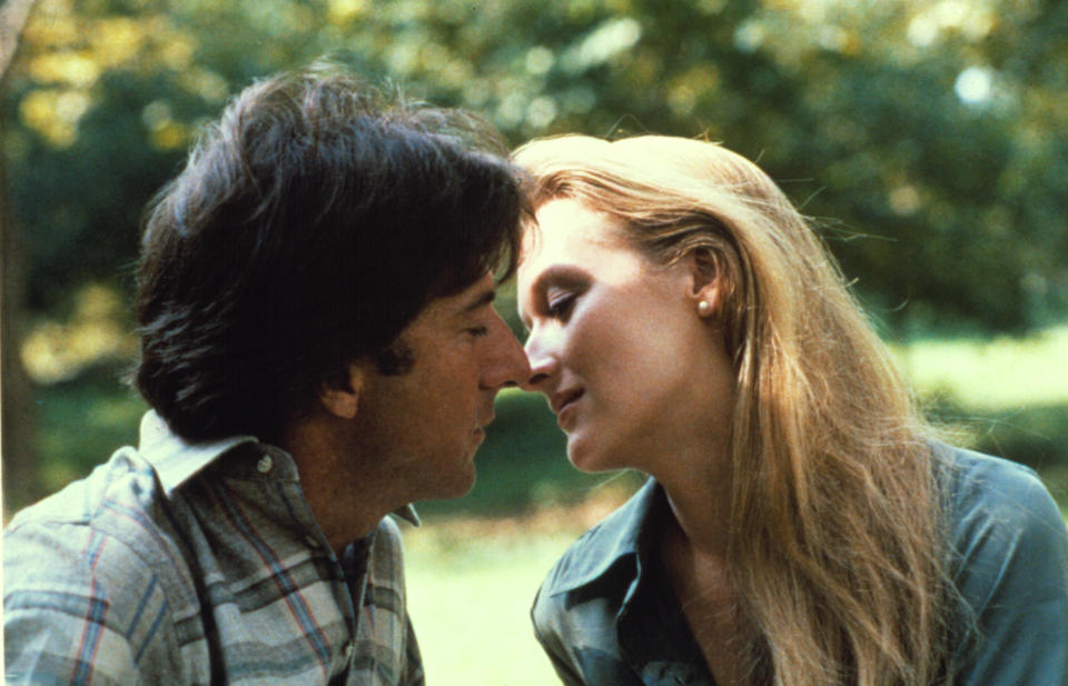 Dustin Hoffman and Meryl Streep share an intimate moment, leaning in for a kiss outdoors in a serene park setting