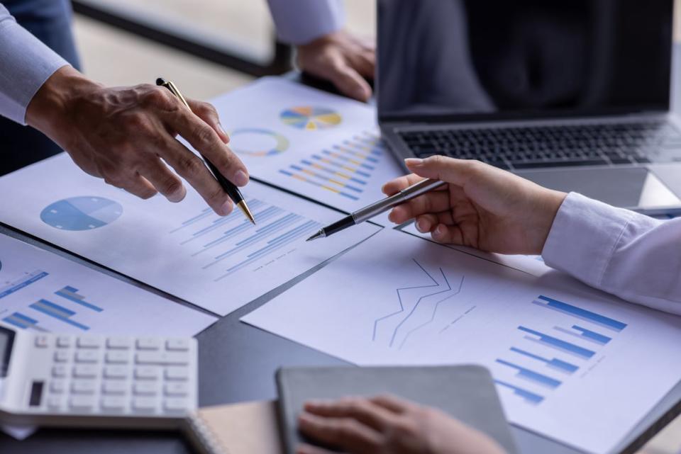 People in a business setting holding pens across documents.