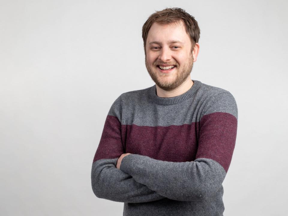 twitch executive lewis mitchell smiles with arms folded against light gray backdrop