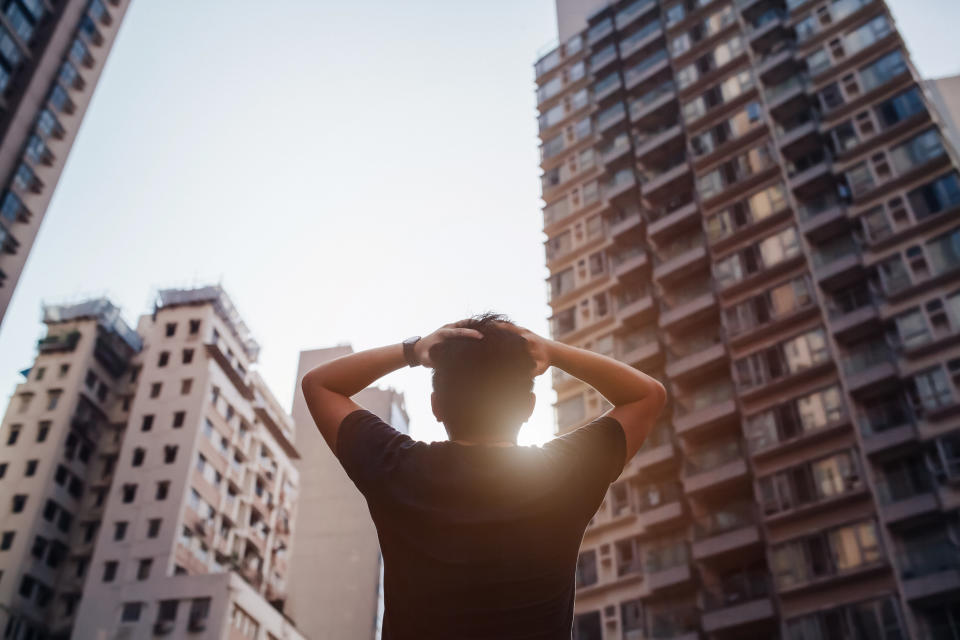 A distraught man holding his head standing in front of the modern city on a fresh early morning.