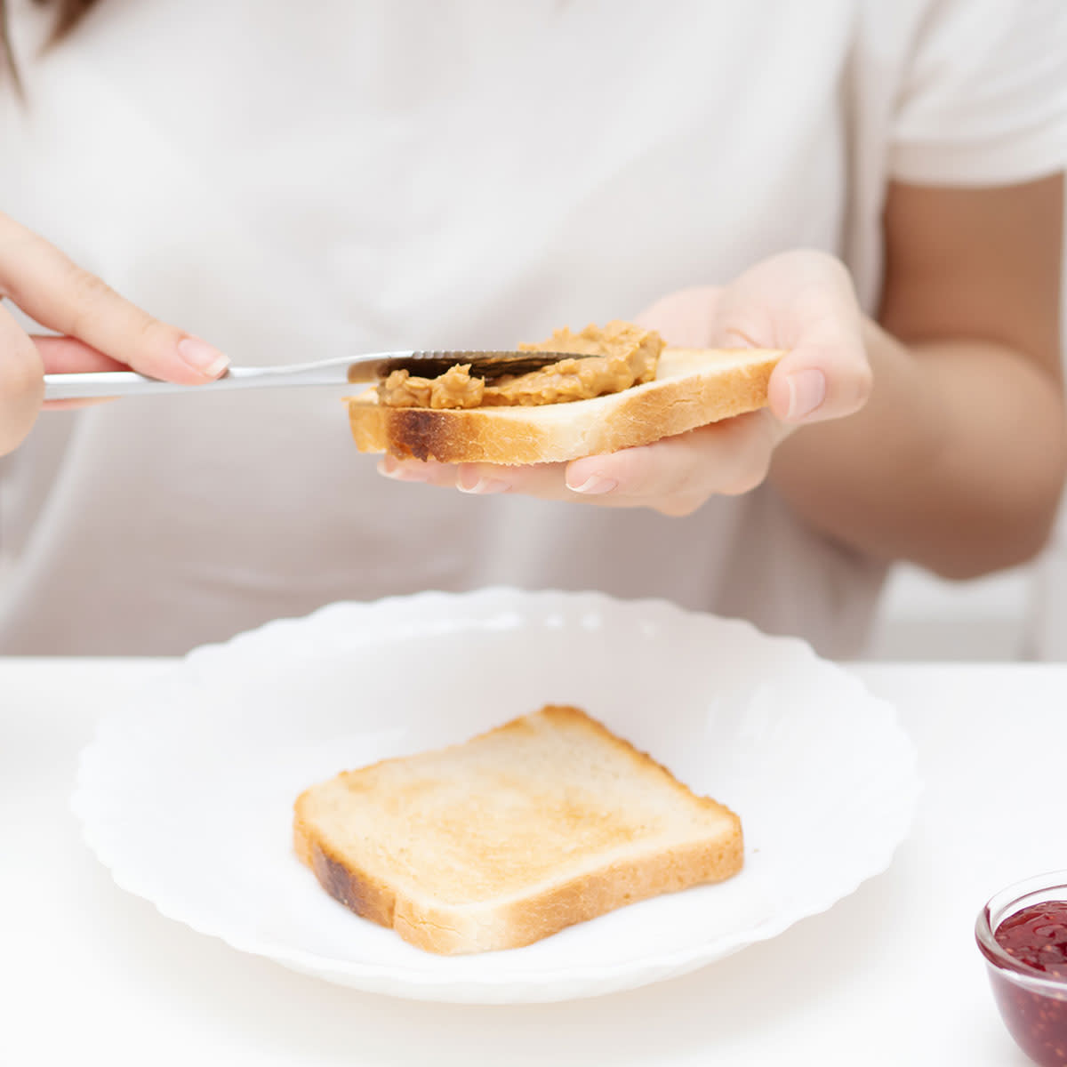 woman adding peanut butter to white toast