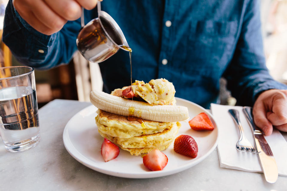 Man pouring maple syrup on pancakes with banana and strawberry.