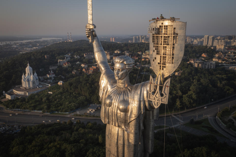 Workers install the Ukrainian coat of arms on the shield in the hand of the country's tallest stature, the Motherland Monument, after the Soviet coat of arms was removed, in Kyiv, Ukraine, Sunday, Aug. 6, 2023. Ukraine is accelerating efforts to erase the vestiges of centuries of Soviet and Russian influence from the public space amid the Russian invasion of Ukraine by pulling down monuments and renaming hundreds of streets to honor home-grown artists, poets, military chiefs, and independence leaders. (AP Photo/Efrem Lukatsky)