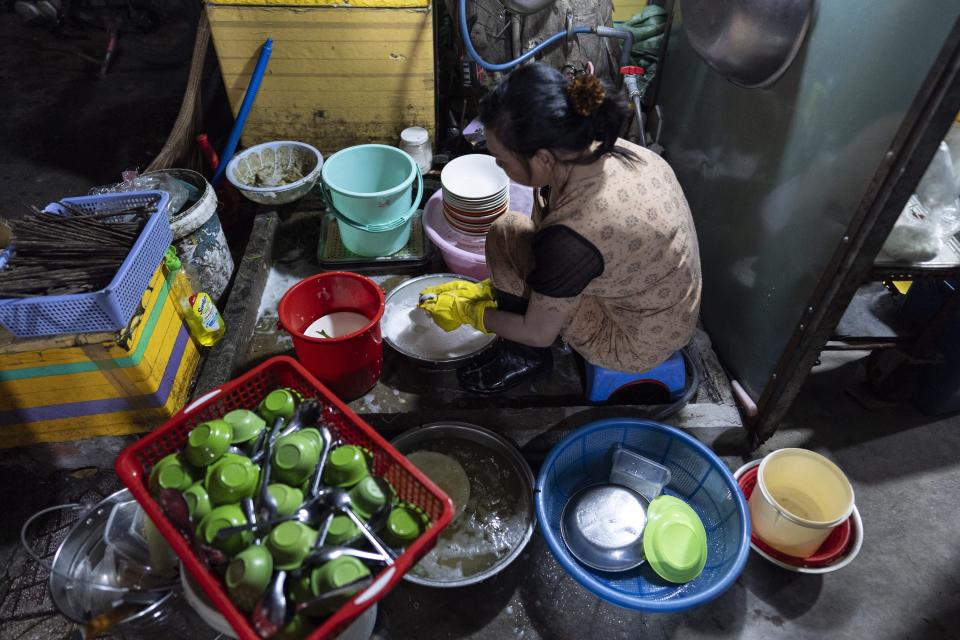 Luong Thi Ut, a migrant from the Mekong Delta who operates a street food stall with her husband, washes dishes outside her apartment after wrapping up for the day in Ho Chi Minh City, Vietnam, on Monday, Jan. 22, 2024. The couple runs the business in the city's industrial zone, a common destination for many migrants from the Mekong Delta in search of a better life. (AP Photo/Jae C. Hong)