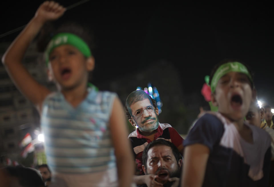 An Egyptian boy wears a a mask with a picture of Morsi sits on his father's shoulders during a protest outside Rabaah al-Adawiya mosque, where of supporters of Egypt's ousted President Mohammed Morsi have installed a camp and hold daily rallies at Nasr City in Cairo, Egypt, Thursday, Aug. 1, 2013. (AP Photo/Khalil Hamra)