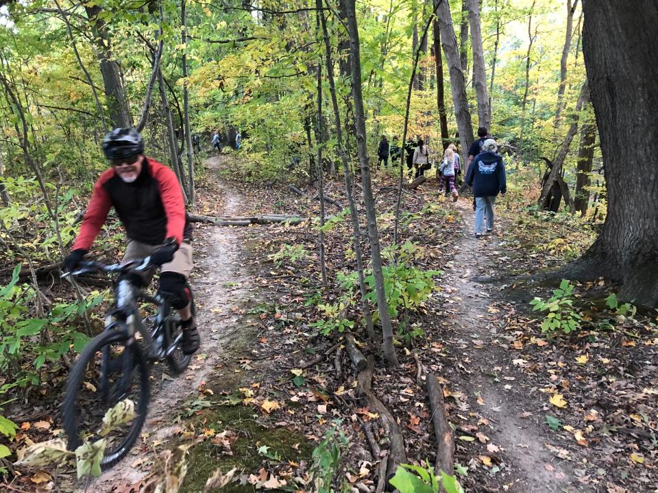 A cyclist rides while others walk Sept. 30 after a ceremony to name the mountain bike trails at Chikaming Township Park and Preserve after Kirk Schrader, who’d conceived them.