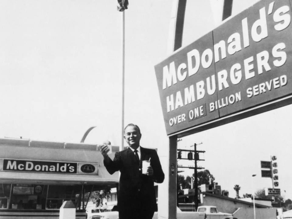 Der Gründer und Vorsitzende der McDonald's Corporation, Ray Kroc, steht mit einem Hamburger und einem Getränk in der Hand vor einer seiner Franchise-Filialen. - Copyright: Bettman/Getty Images