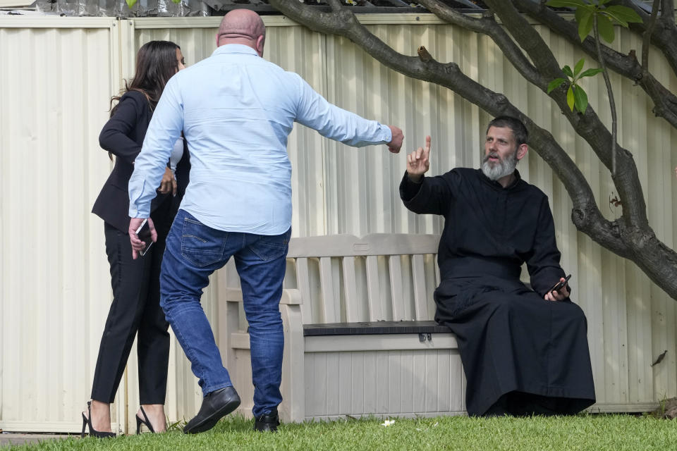 Father Daniel Kochou, right, gestures as he speaks with people, across the road from the Christ the Good Shepherd church in suburban Wakely in western Sydney, Australia, Tuesday, April 16, 2024. Australian police say a knife attack in Sydney that wounded a bishop and a priest during a church service as horrified worshippers watched online and in person, and sparked a riot was an act of terrorism. (AP Photo/Mark Baker)