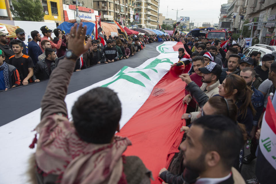 Anti government protesters carry a big Iraqi flag and chant anti Iran and anti U.S. slogans during the ongoing protests in Tahrir square, Baghdad, Iraq, Friday, Jan. 10, 2020. (AP Photo/Nasser Nasser)