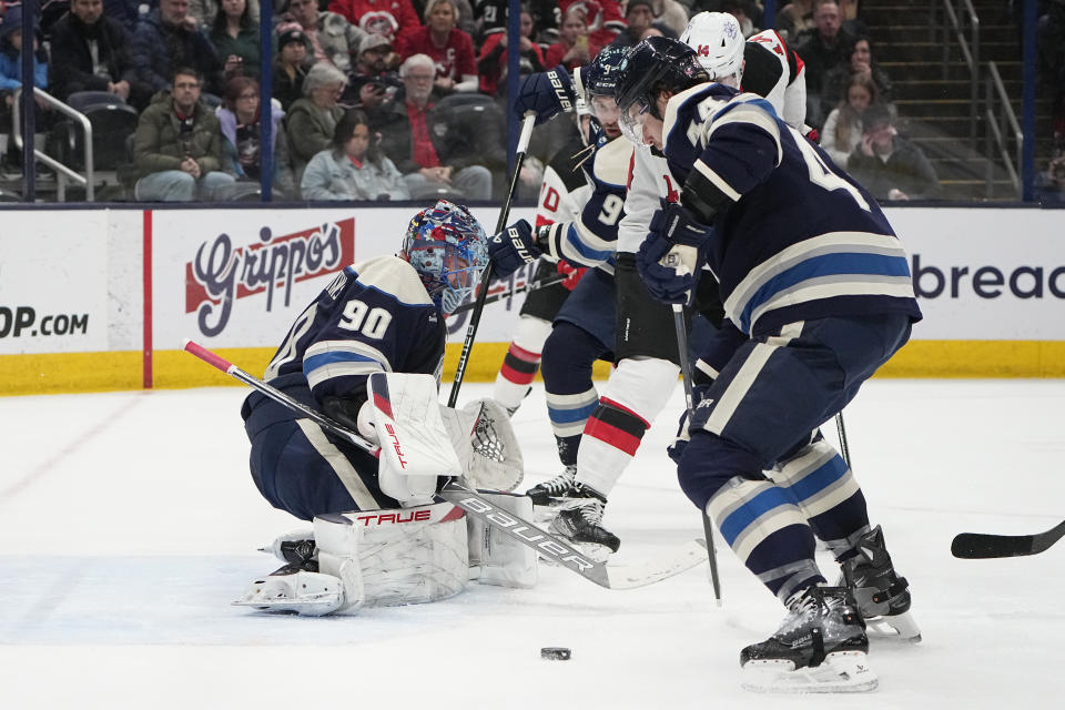 Columbus Blue Jackets goaltender Elvis Merzlikins blocks a shot by New Jersey Devils right wing Nathan Bastian (14), between defenseman Ivan Provorov (9) and defenseman Erik Gudbranson (44) during the first period of an NHL hockey game Friday, Jan. 19, 2024, in Columbus, Ohio. (AP Photo/Sue Ogrocki)