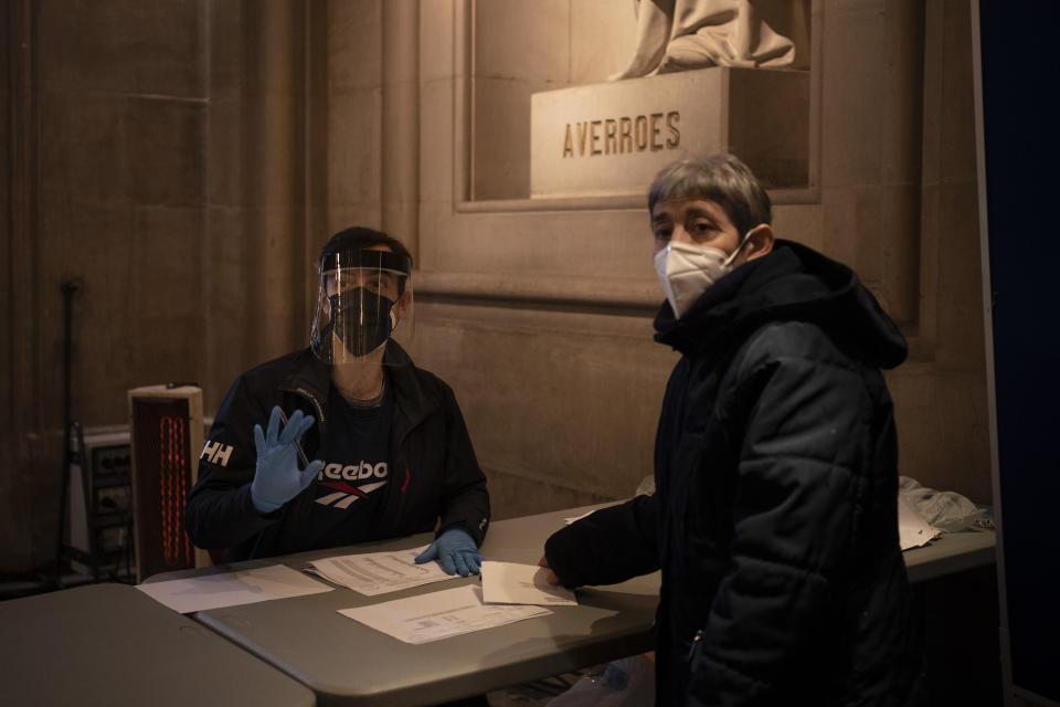 A man working at a polling station in the Barcelona University gestures to people waiting in line to cast their vote for the Catalan regional election in Barcelona, Spain, Sunday, Feb. 14, 2021. Over five million voters are called to the polls on Sunday in Spain's northeast Catalonia for an election that will measure the impact of the coronavirus pandemic on the restive region's secessionist movement. (AP Photo/Felipe Dana)