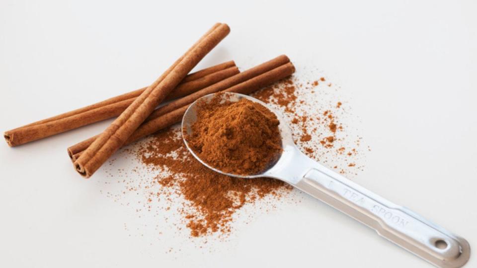 A teaspoon of cinnamon beside cinnamon sticks on white background 