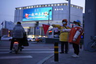 A young volunteer helps to direct traffic at a junction where a screen is showing an ad for the 2022 Winter Olympics in Beijing on Thursday, Feb. 10, 2022. The possibility of a large outbreak in the bubble, potentially sidelining athletes from competitions, has been a greater fear than any leakage into the rest of China. (AP Photo/Ng Han Guan)