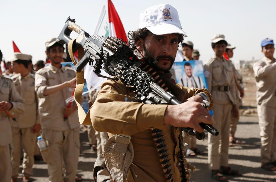 A Houthi fighter carries a machine gun in front of scout team members carrying Yemeni and Palestinian flags (Getty Images)