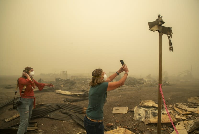 GREENVILLE, CA - AUGUST 07, 2021: Kelly Tan, 59, left, looks on as her sister, Tiffany Lozano, 44, photographs melted street signs on Main St. in Greenville, caused by the extreme temperature of the Dixie Fire that destroyed most of the town. Lozano is a resident of nearby Quincy and Tan is a resident of nearby Taylorsville. (Mel Melcon / Los Angeles Times)