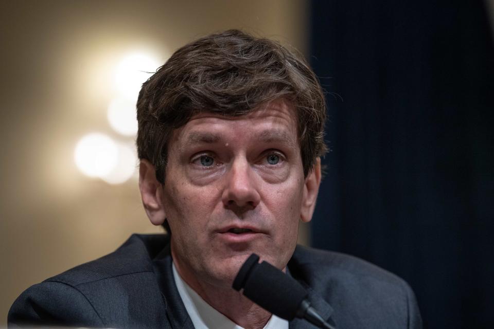 A man wearing a suit is seen in front of a microphone and looking ahead