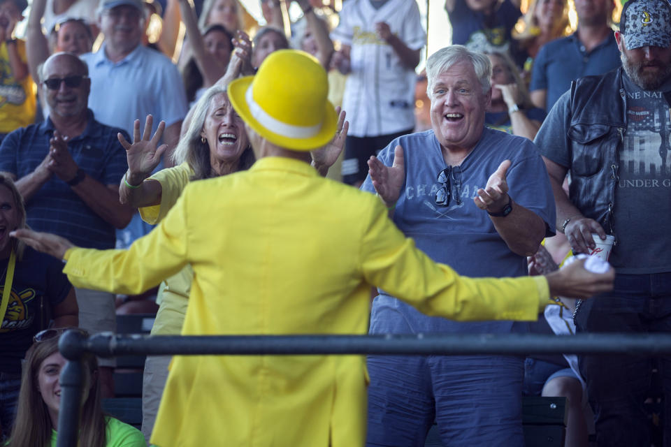 Savannah Bananas fan Chuck Henze, right, and his wife, Marian Henze, left, of Wilmington, N.C., cheer for Bananas owner Jesse Cole, center, during T-shirt giveaway during the first inning of the team's baseball game against the Florence Flamingos, Tuesday, June 7, 2022, in Savannah, Ga. (AP Photo/Stephen B. Morton)