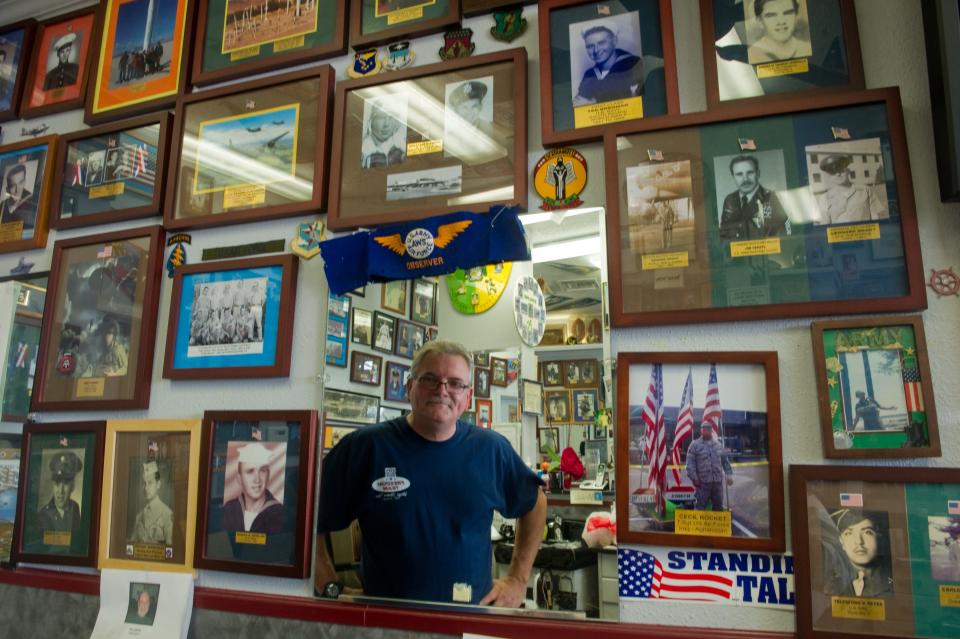 Village Barbershop owner Bobby Page is reflected in a mirror among some of the many photos of veterans he has up on the walls of his shop at Lincoln Center in Stockton in 2014.