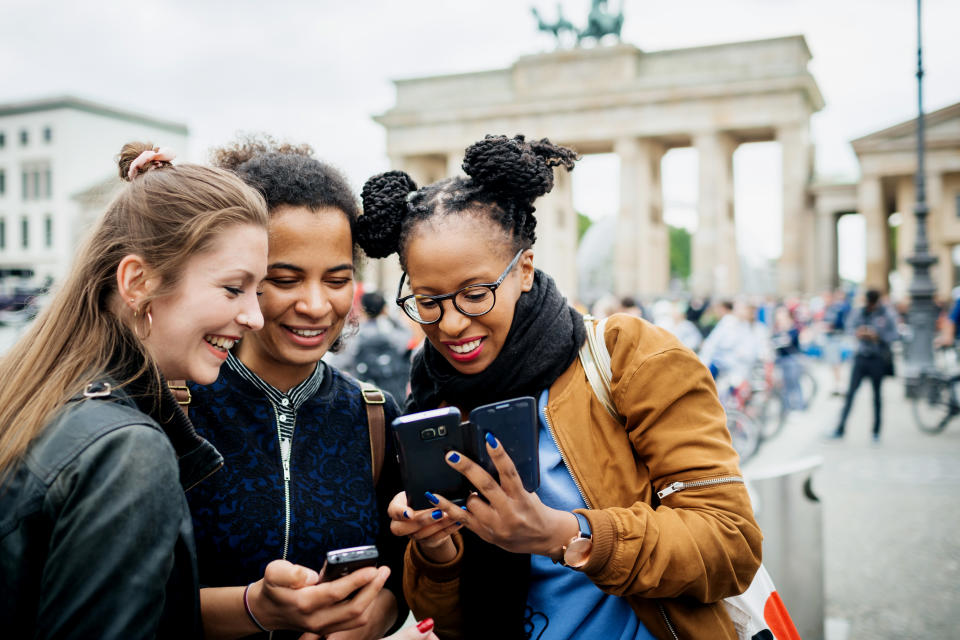 A group of friends travelling together are exploring the local tourist attractions and architecture, they stop for a moment to look over recent photos on their phones.