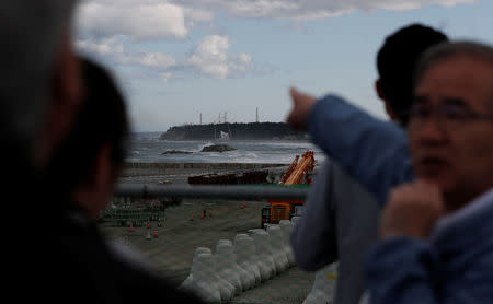 Katsumi Miyaguchi (R), deputy mayor of Namie town, points to cranes and chimneys of Tokyo Electric Power Co's (TEPCO) tsunami-crippled Fukushima Daiichi nuclear power plant, as he guides tourists from Tokyo's universities at an area devastated by the March 11, 2011 earthquake and tsunami in Namie town, Fukushima prefecture, Japan May 19, 2018. Picture taken May 19, 2018. REUTERS/Toru Hanai