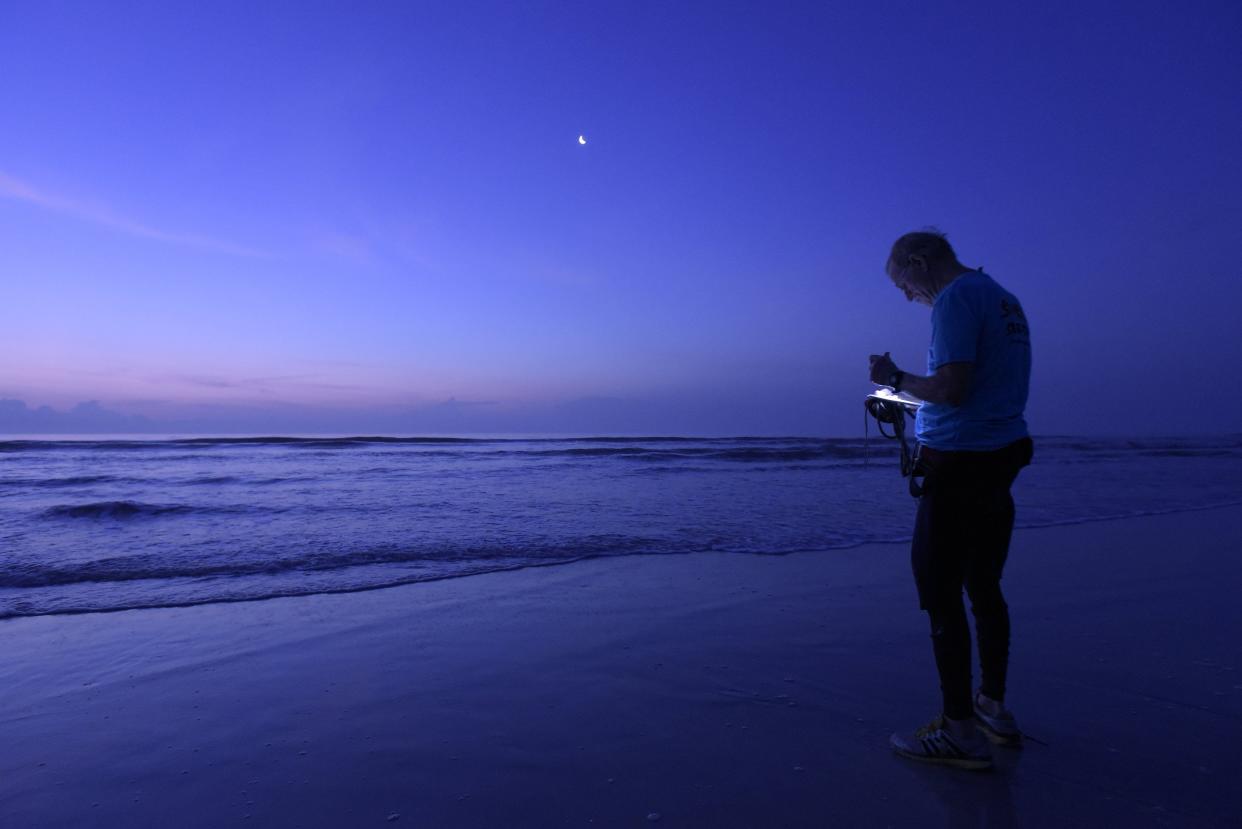 Bill Longenecker uses a small flashlight to read the thermometer that he threw into the surf to check the water temperature for his morning surf report in this 2015 file photo.