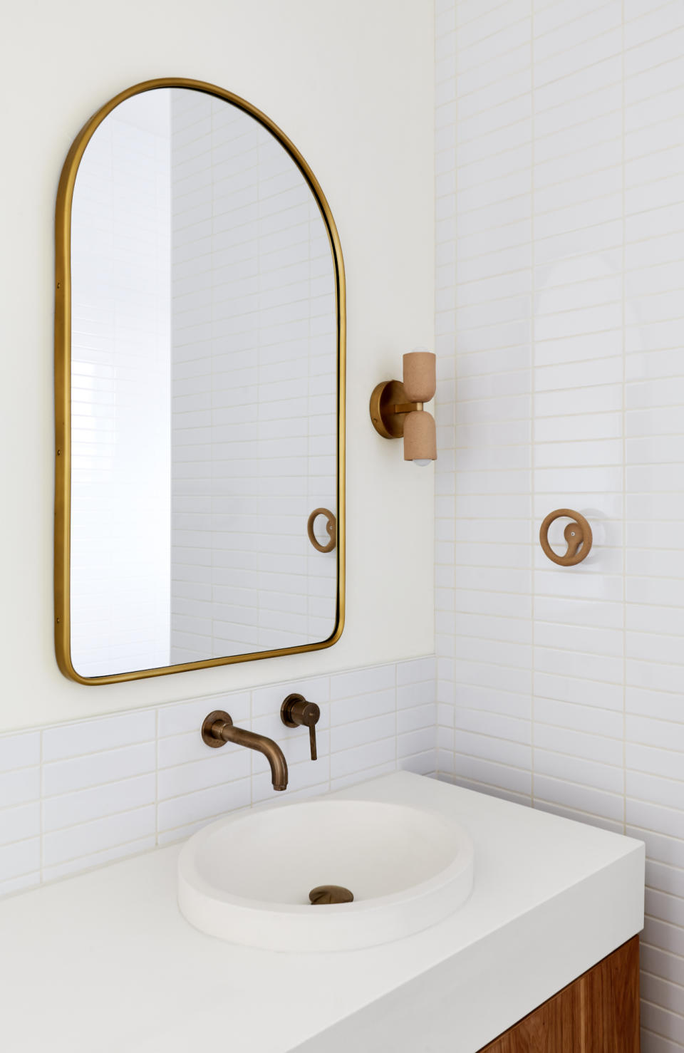 White bathroom with white tiled walls, white countertop, brass tap and mirror and ceramic wall light and towel hook