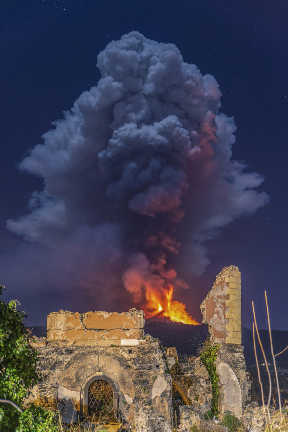 Flames and smoke billowing from a crater, as seen from the eastern side of the Mt Etna volcano, are framed by the remains of a building that collapsed after an October 1984 quake in Fleri, Sicily, Wednesday night, Feb. 24, 2021. Europe's most active volcano has been steadily erupting since last week, belching smoke, ash, and fountains of red-hot lava. (AP Photo/Salvatore Allegra)