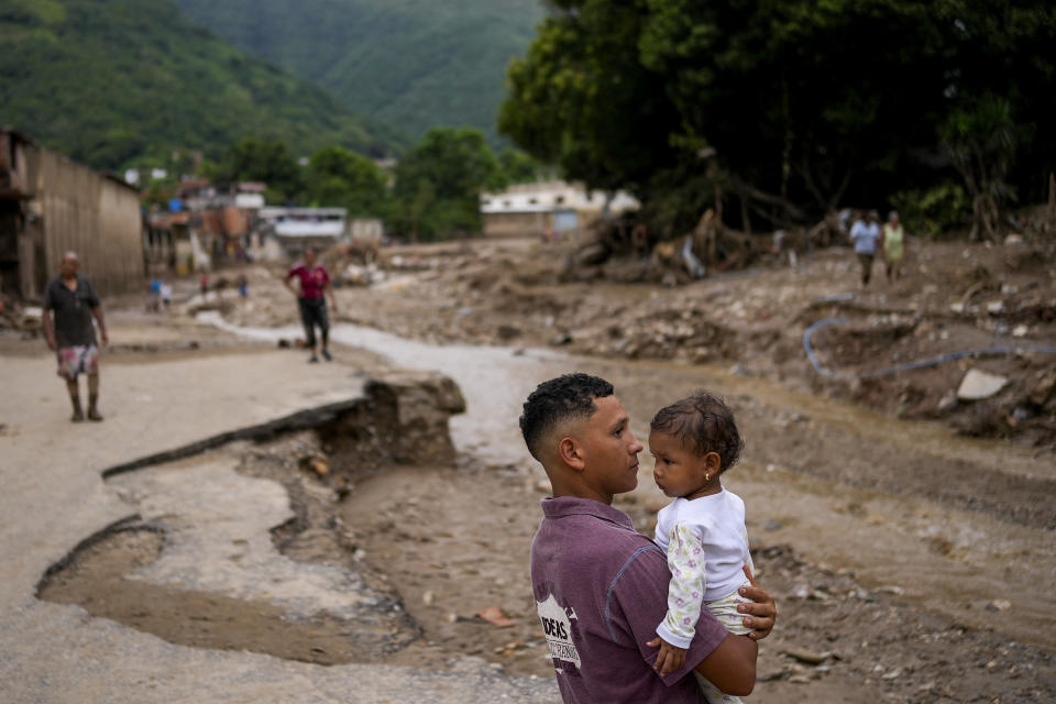 A man holds his daughter next to an overflow revine that triggered flooding in Las Tejerias, Venezuela, Sunday, Oct. 9, 2022. At least 22 people died due to flash floods, Vice President Delcy Rodríguez said. (AP Photo/Matias Delacroix)