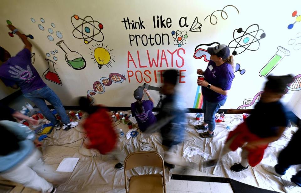 Westerly Hills Academy students pass by Novant Health employees painting a mural on Friday, April 19, 2024. Novant Health employees joined employees from other local companies for the 19th Charlotte Playground Build. The playground build is presented by United Way of Greater Charlotte that brings together companies across the community to build a new playground for a local Charlotte-Mecklenburg elementary school.