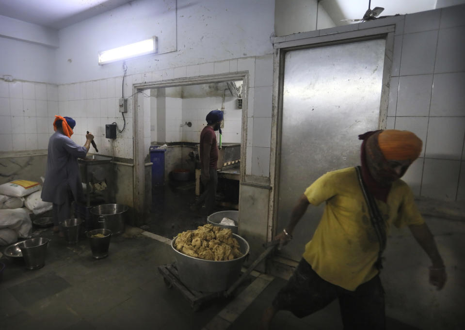 A Sikh volunteer carries dough for making chapati, thin unleavened bread, as others prepare spices in the kitchen hall of the Bangla Sahib Gurdwara in New Delhi, India, Sunday, May 10, 2020. The Bangla Sahib Gurdwara has remained open through wars and plagues, serving thousands of people simple vegetarian food. During India's ongoing coronavirus lockdown about four dozen men have kept the temple's kitchen open, cooking up to 100,000 meals a day that the New Delhi government distributes at shelters and drop-off points throughout the city. (AP Photo/Manish Swarup)