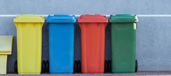 Four colorful garbage bins against a wall.