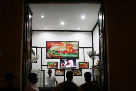 People watch a television installed under advertisements of a coffee shop in Havana, Cuba, May 26, 2016. REUTERS/Alexandre Meneghini