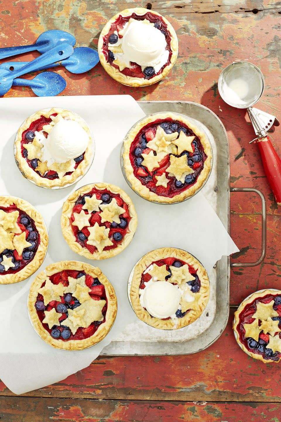 seven mini stars berry pies arranged on a metal serving tray with a scoop of ice cream on two of them