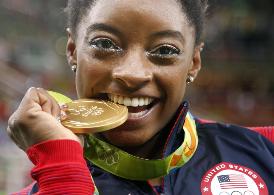 FILE - United States' Simone Biles bites her gold medal for the artistic gymnastics women's individual all-around final at the 2016 Summer Olympics in Rio de Janeiro, Brazil, Aug. 11, 2016. (AP Photo/Dmitri Lovetsky, File)