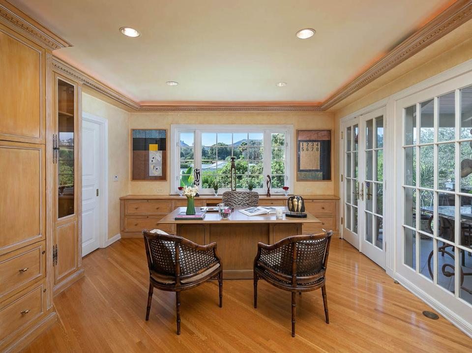 an office with a desk, three chairs, and windows