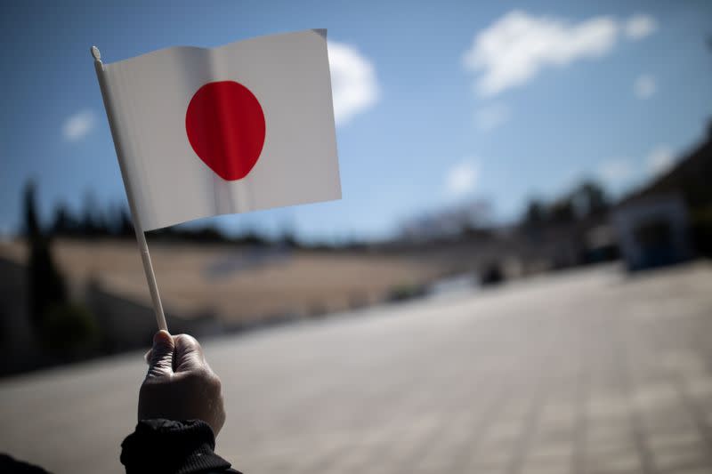 A man wearing protective plastic gloves waves a Japanese flag outside the Panathenaic Stadium in Athens