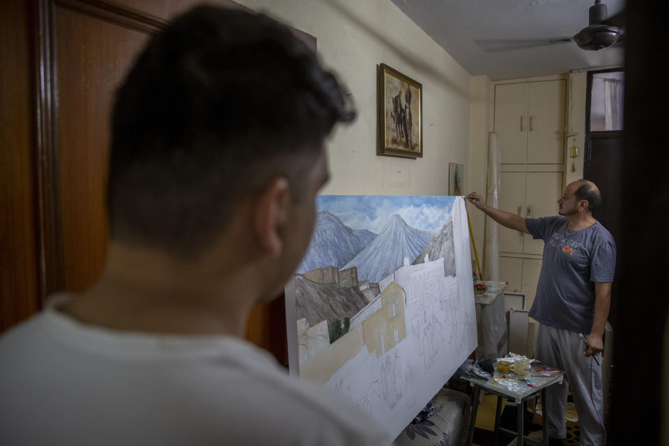 Mohammad Hassan watches as his father, Akbar Farhad, an Afghan artist, paints an old Kabul market and the ruins of "Bala-e- Hissar," or the High Fort, an ancient citadel that housed Afghan rulers for centuries, inside a rented accommodation in New Delhi, India, on Aug. 13, 2021. Akbar Farhad has been living in New Delhi since 2018. He left Kabul after facing threats from insurgents demanding he close his studio. Like thousands of other Afghan refugees in India, their plans to someday return home were dashed by the Taliban's shockingly swift takeover of the country. (AP Photo/Altaf Qadri)