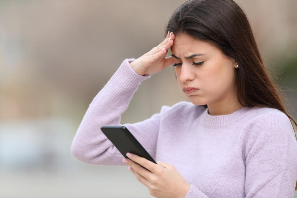 Una mujer mira whatsapp en su celular con cara de frustrada  (Getty Images)