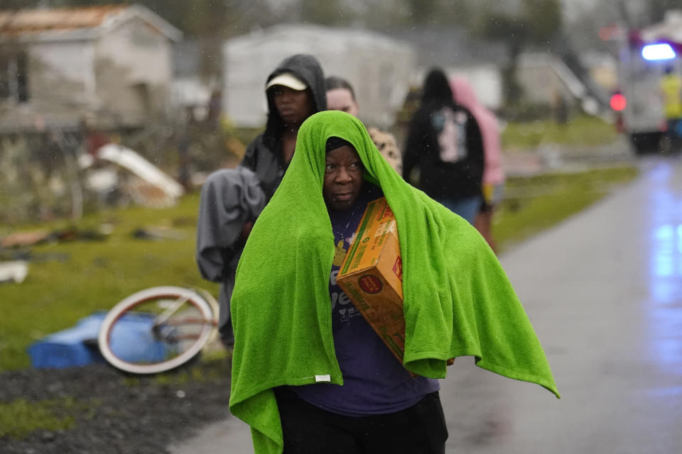 A woman with a towel over her head to try to stay dry walks in the rain after she arrived to help her niece, whose home was destroyed.