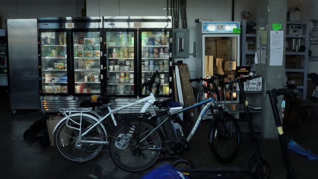 A delivery bike parked in front of fridges filled with grocery items in a warehouse.