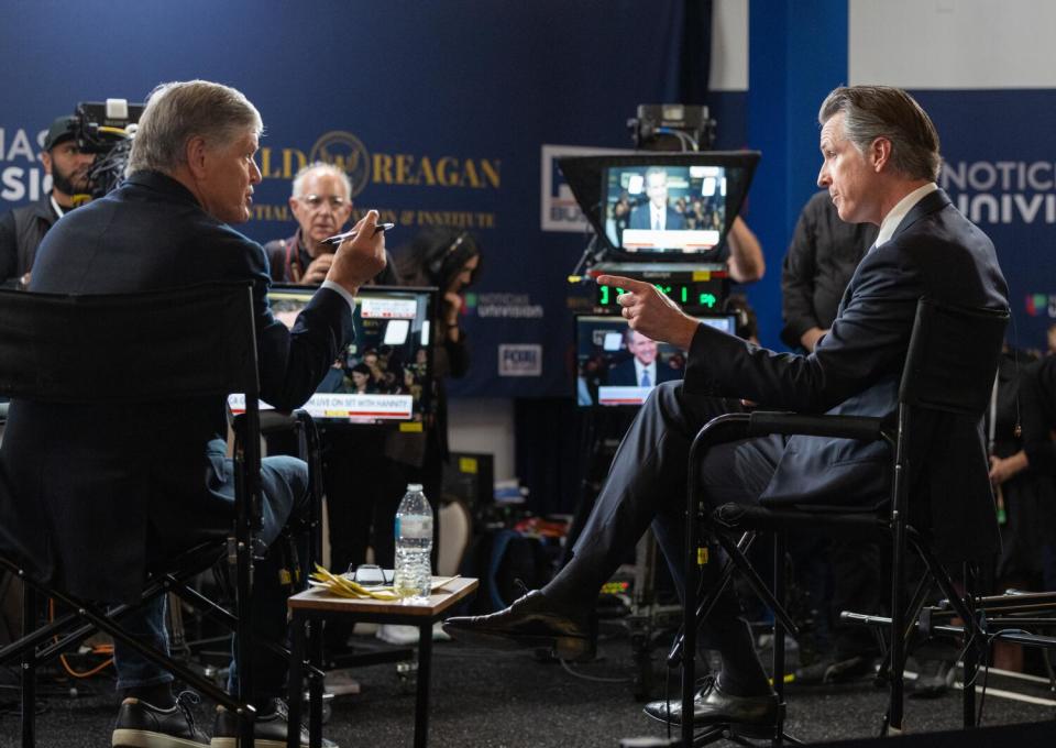 A man in a dark suit, right, gestures toward another man seated across from him