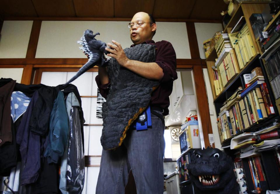 In this Thursday, May 1, 2014 photo, Kazuya Haraguchi, 45, a technician for film reel, wearing a part of real Godzilla costume he purchased in auction, holds the monster's figure at his apartment in Tokyo. Godzilla-lovers in this nation where the stomping all began say their iconic hero falls into a special phantasmal category called “kaiju,” different from more mundane monsters like King Kong or Frankenstein. And the Hollywood version is no kaiju, said Haraguchi who collects Godzilla goods, including a 100,000 yen ($1,000) complete DVD collection from Toho Studios, which came with a huge fangs-baring Godzilla head. (AP Photo/Junji Kurokawa)