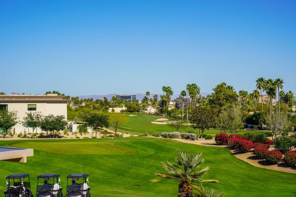 A golf course lined with palm trees with mountains in the background, clear blue skies