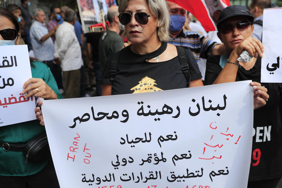A protester holds an Arabic placard that reads: "Lebanon is besieged and a hostage, yes to neutrality, yes for an international conference, yes for implementing international resolutions," during a demonstration of solidarity with Judge Tarek Bitar who is investigating last year's deadly seaport blast, outside a court building in Beirut, Lebanon, Wednesday, Sept. 29, 2021. Hundreds of Lebanese, including families of the Beirut port explosion victims, rallied Wednesday outside the court of justice in support of Bitar after he was forced to suspend his work. Bitar is the second judge to take on the complicated investigation.(AP Photo/Hussein Malla)