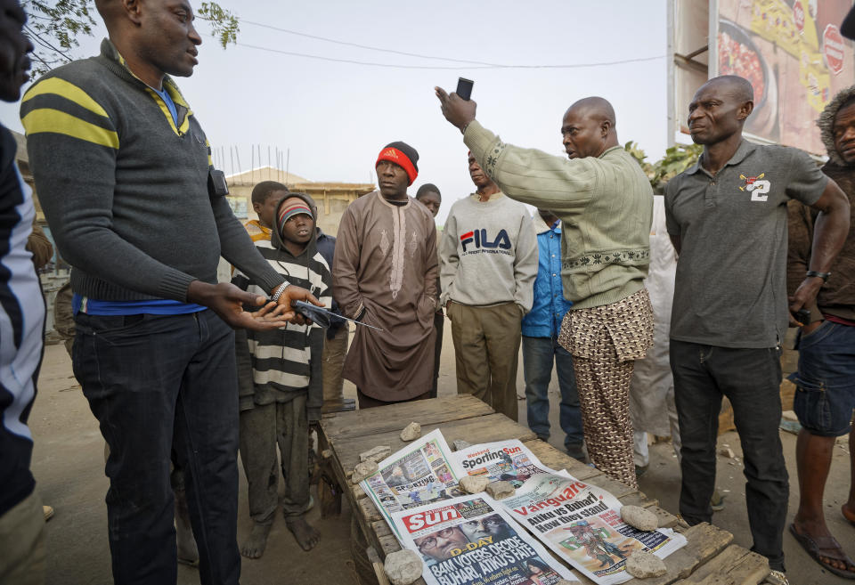 Nigerians discuss the overnight developments at a newspaper stand selling copies of papers that printed before the postponement was announced, in the morning in Kano, in northern Nigeria Saturday, Feb. 16, 2019. Nigeria's electoral commission delayed the presidential election until Feb. 23, making the announcement a mere five hours before polls were set to open Saturday. (AP Photo/Ben Curtis)