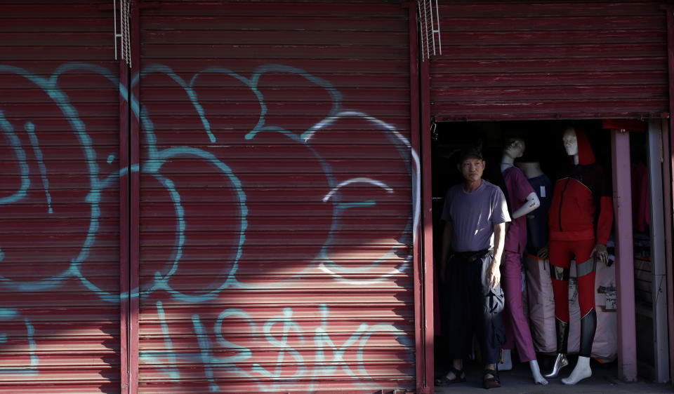 Teeyung Chang looks out the door of his shuttered clothing store near the border Tuesday, July 21, 2020, in Calexico, Calif. Forced to shut his doors to shoppers as the coronavirus cases surged, Chang is unsure if his Divas Fashions store will survive. (AP Photo/Gregory Bull)