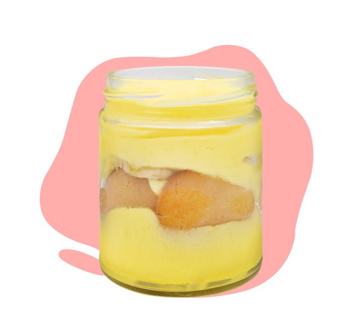 A simple portion of banana pudding with vanilla wafers in a clear glass jar on a pink blob background