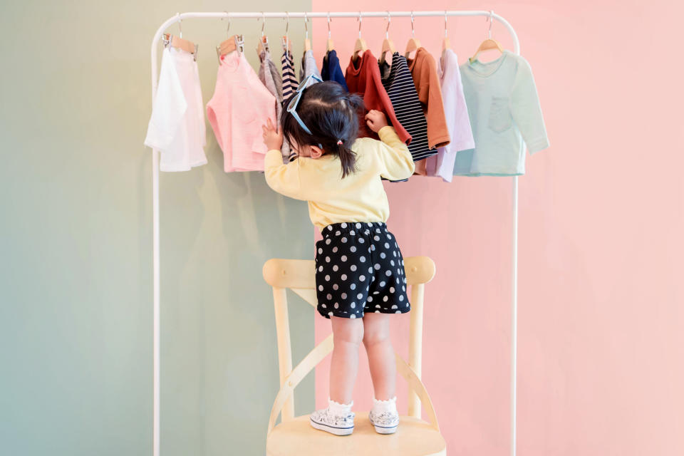 A female toddler browses through a rack of clothes.