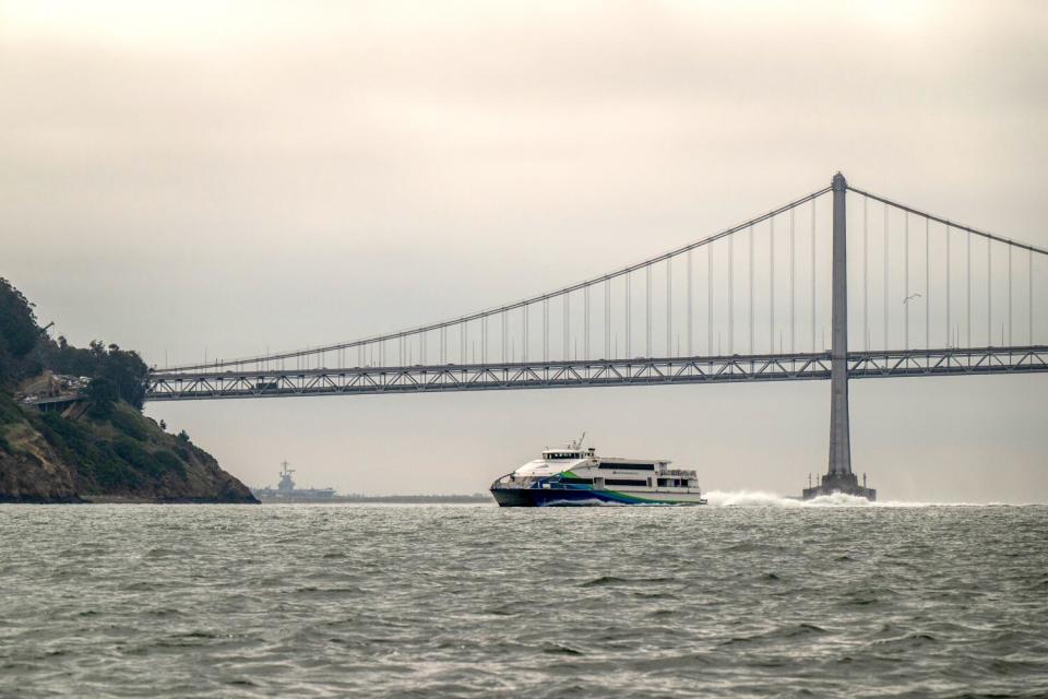 A fast ferry sails across San Francisco Bay under a cloudy sky.