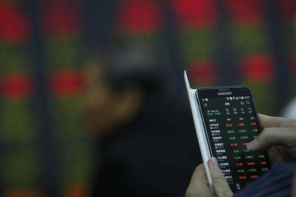 A man checks stock prices through his smartphone at a brokerage house in Beijing, Wednesday, Oct. 24, 2018. Asian markets are mixed on Wednesday after U.S. companies, including those that outperformed in the third quarter, cautioned against escalating a trade dispute with China. (AP Photo/Andy Wong)